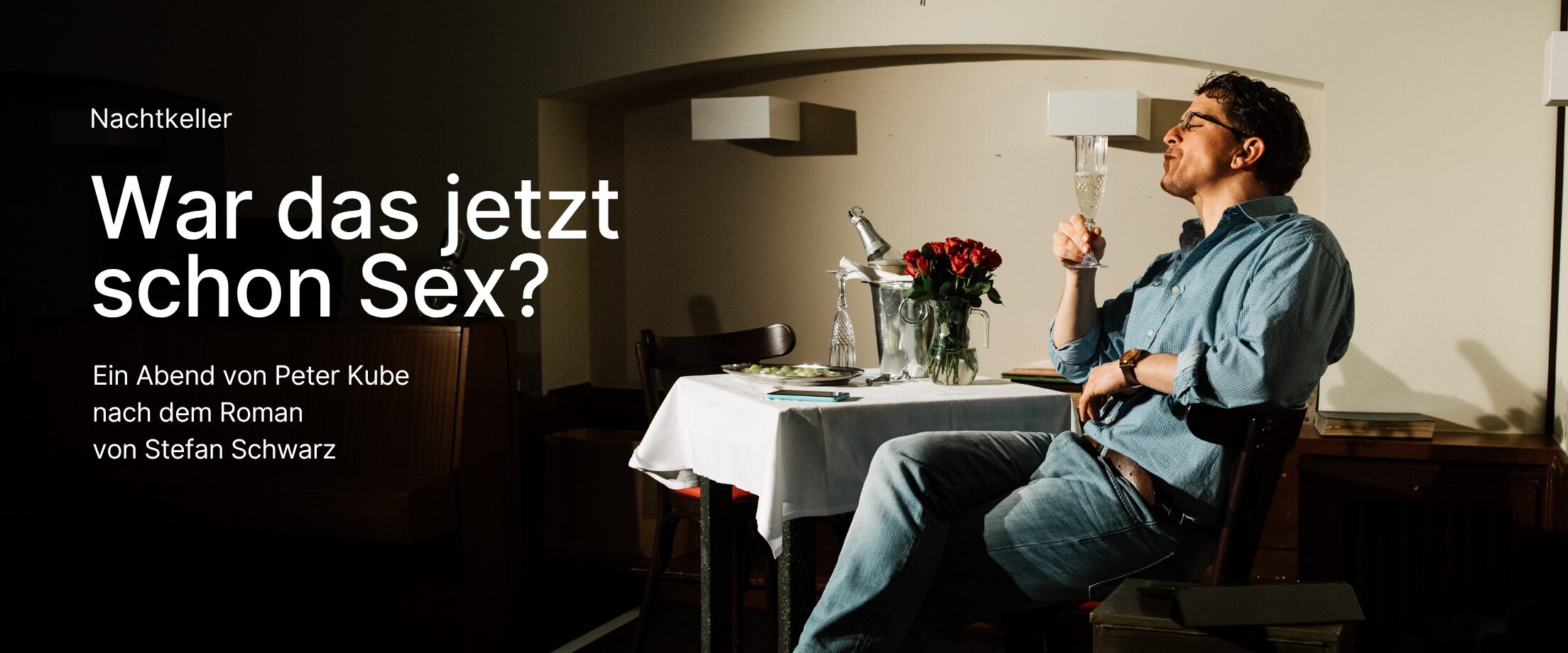 Ein Mann sitzt mit einem Glas Sekt an einem gedeckten Tisch mit Rosen darauf.