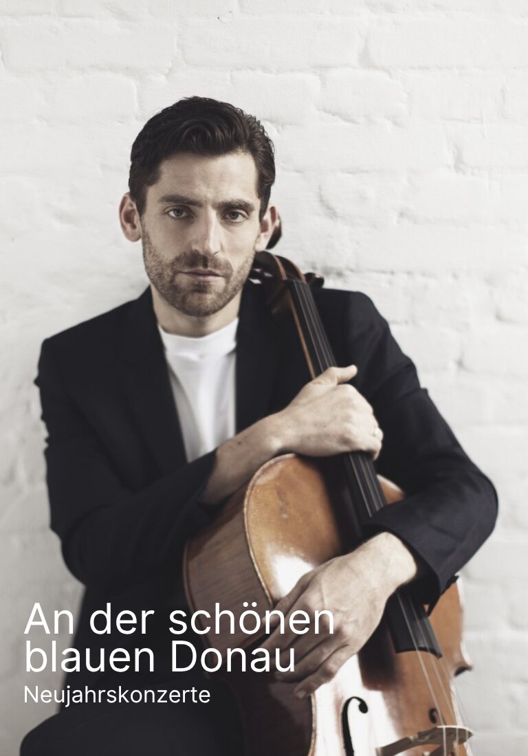 Arthur Hornig vor einer weißen Wand mit einem Cello vor sich stehend