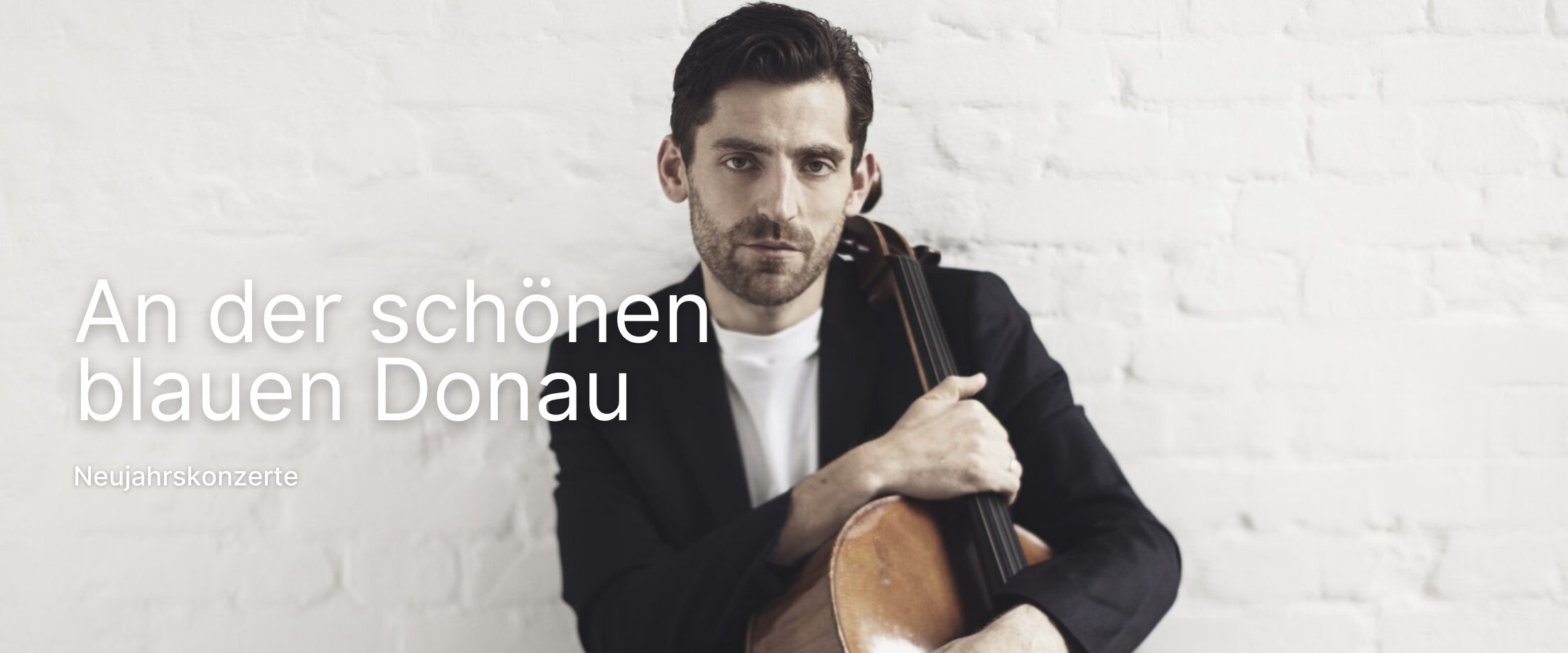 Arthur Hornig vor einer weißen Wand mit einem Cello vor sich stehend