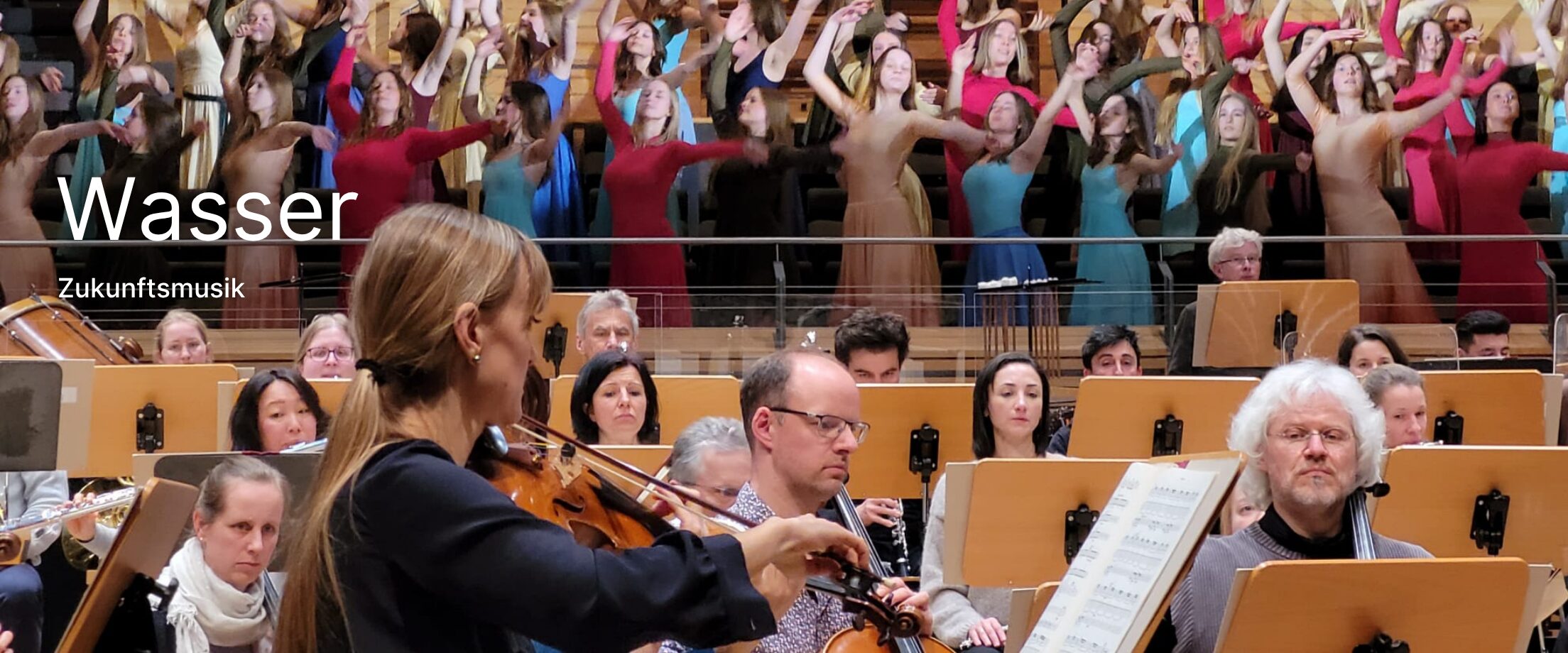 Die Neubrandenburger Philharmonie spielt im Vordergrund, dahinter stehen junge Frauen mit schwingenden Armen